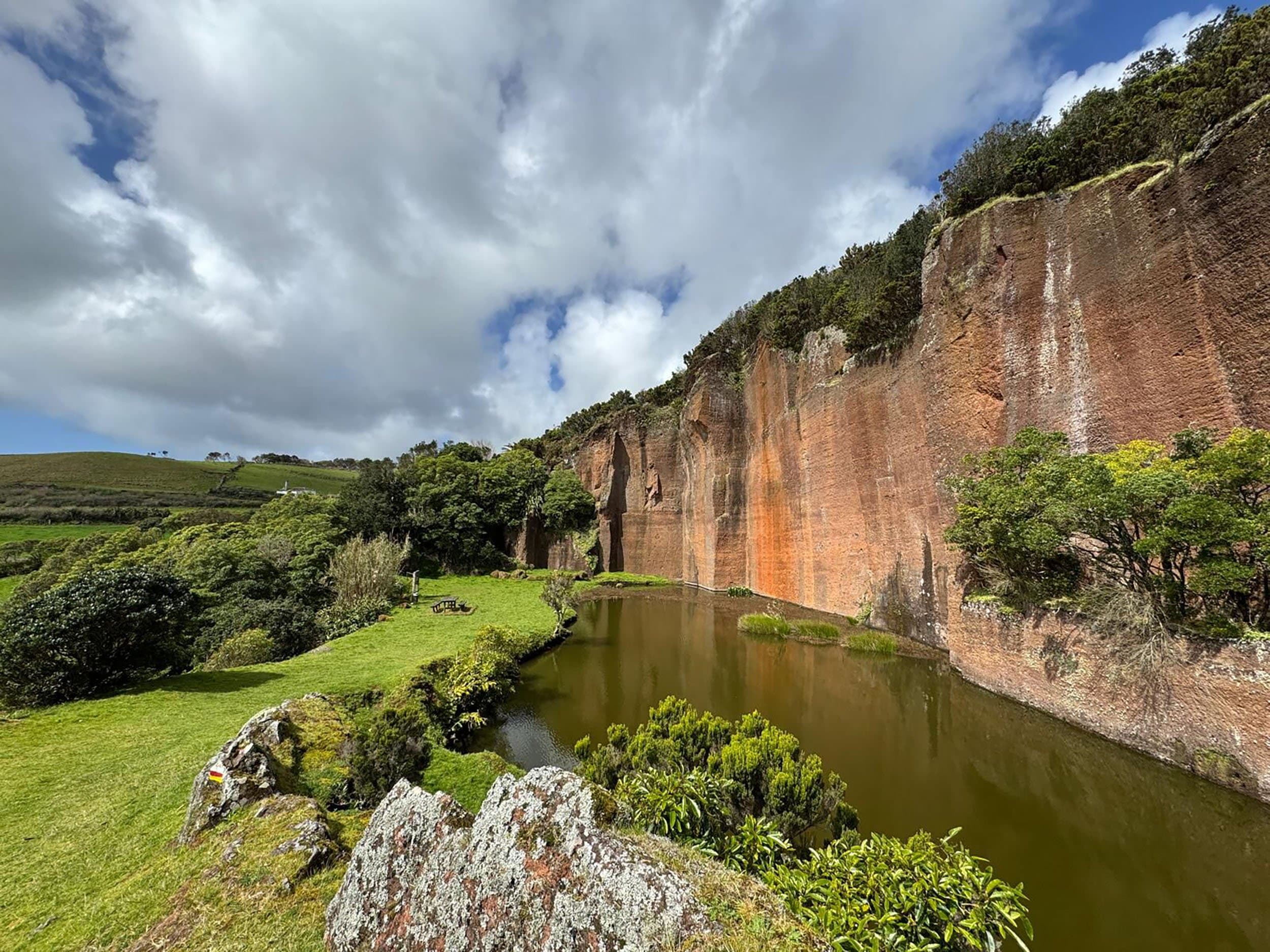 a high cliff next to a green pond