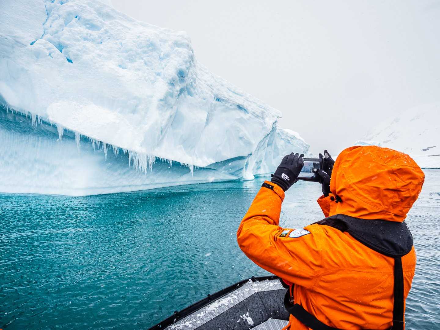 A person in a parka photographs a giant iceberg