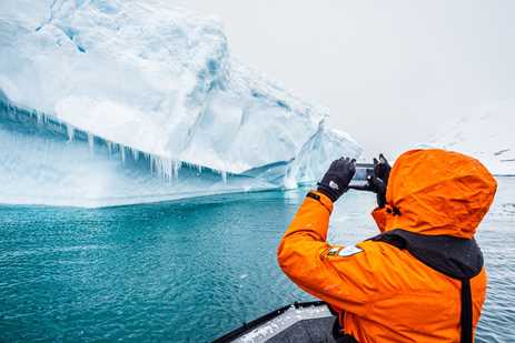 A person in a parka photographs a giant iceberg