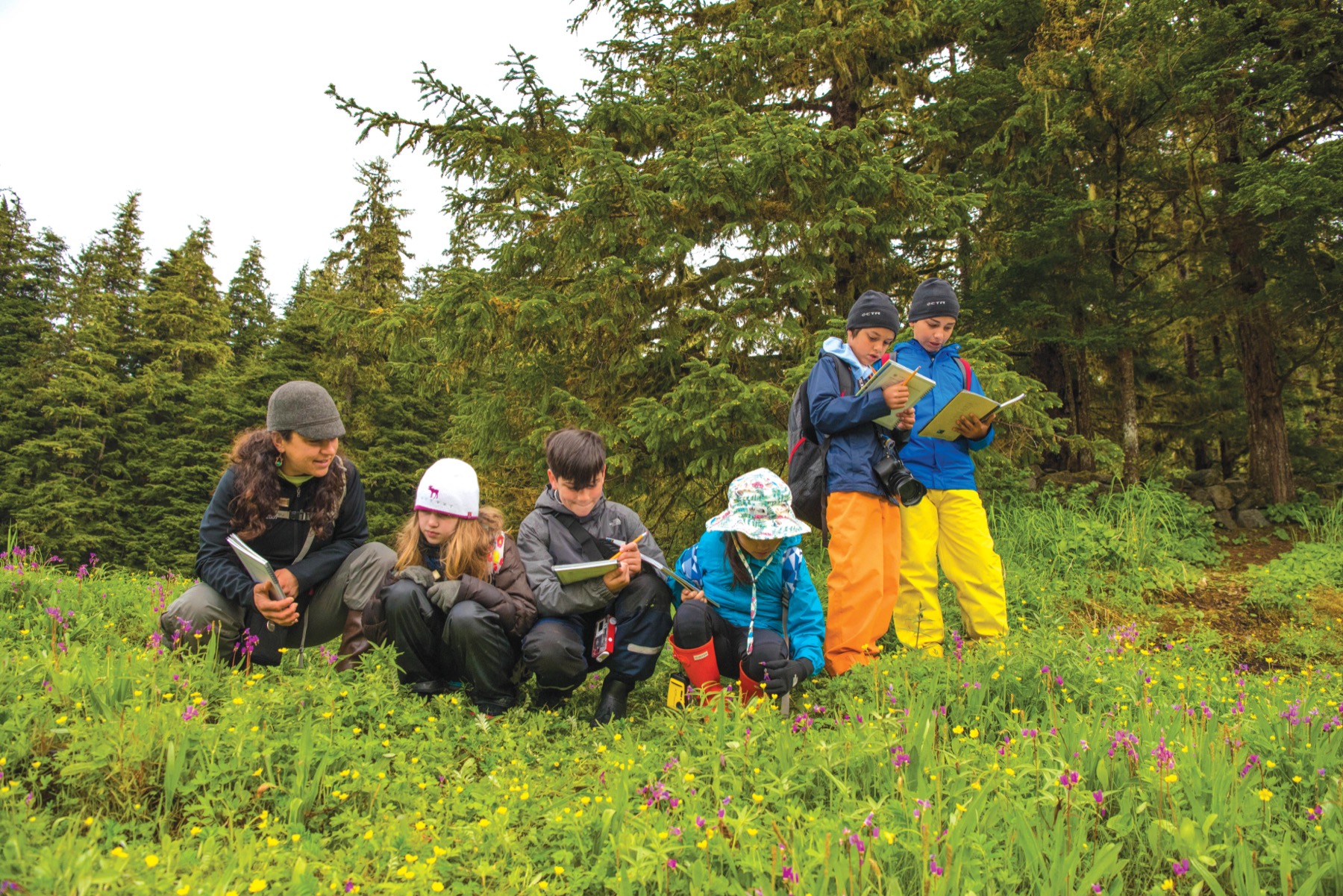 A group of children study some written material while out in the woods