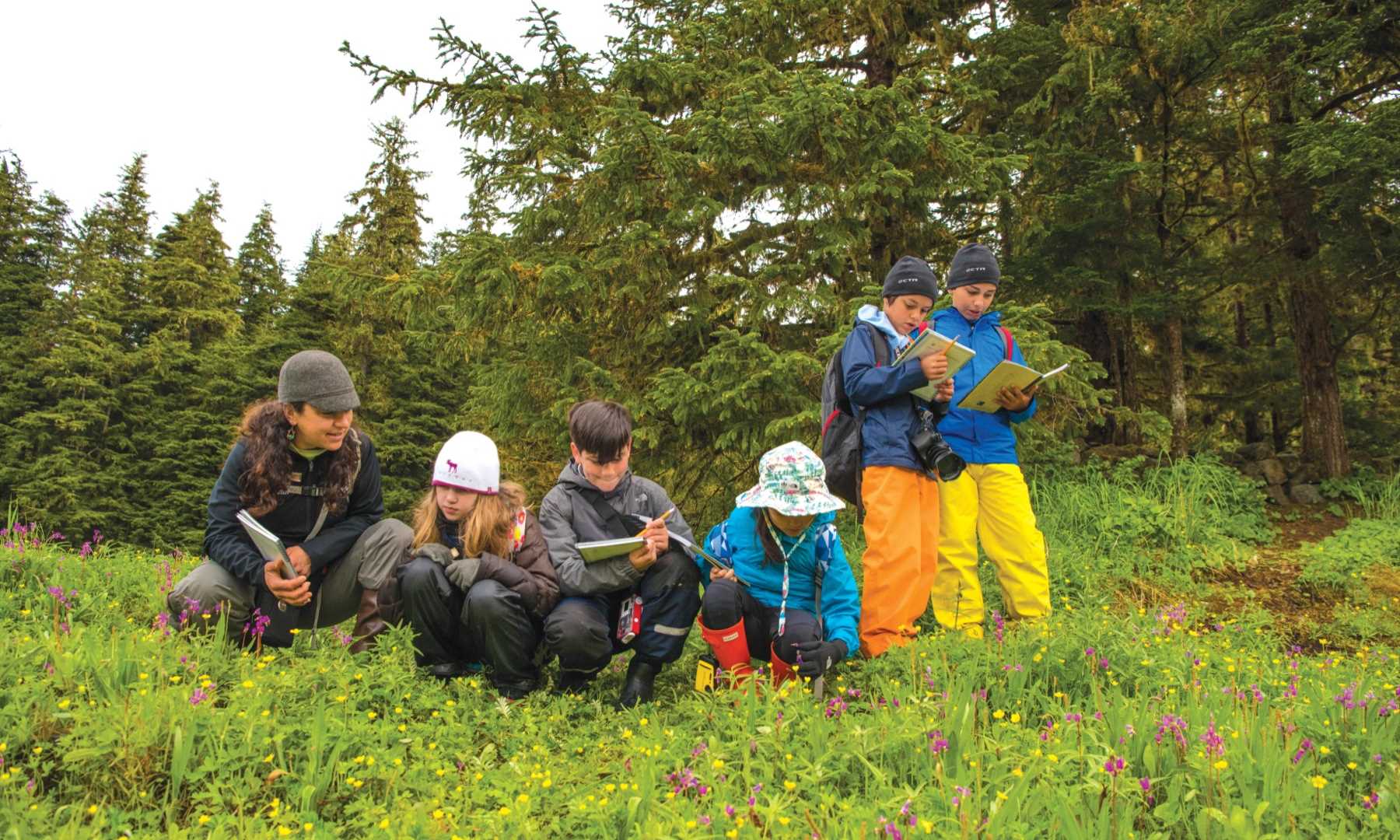 A group of children study some written material while out in the woods