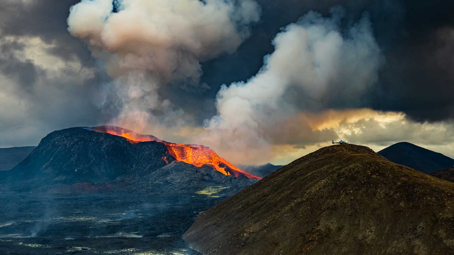 Erupting volcano in Iceland with helicopter on nearby peak