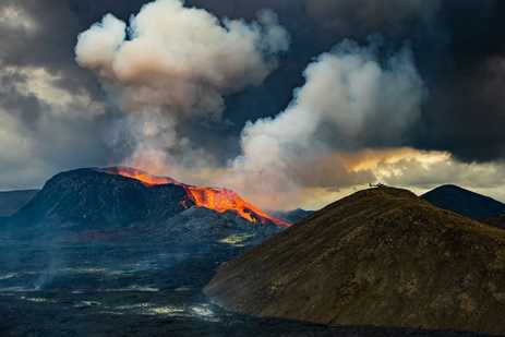 Erupting volcano in Iceland with helicopter on nearby peak