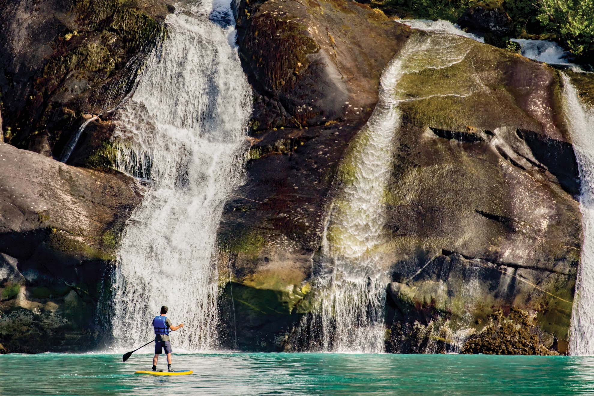 A solo paddleboarder stops in front of a waterfall