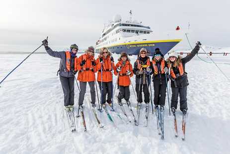 A group of guests cross country skiing pose in front the National Geographic Orion in Antarctica
