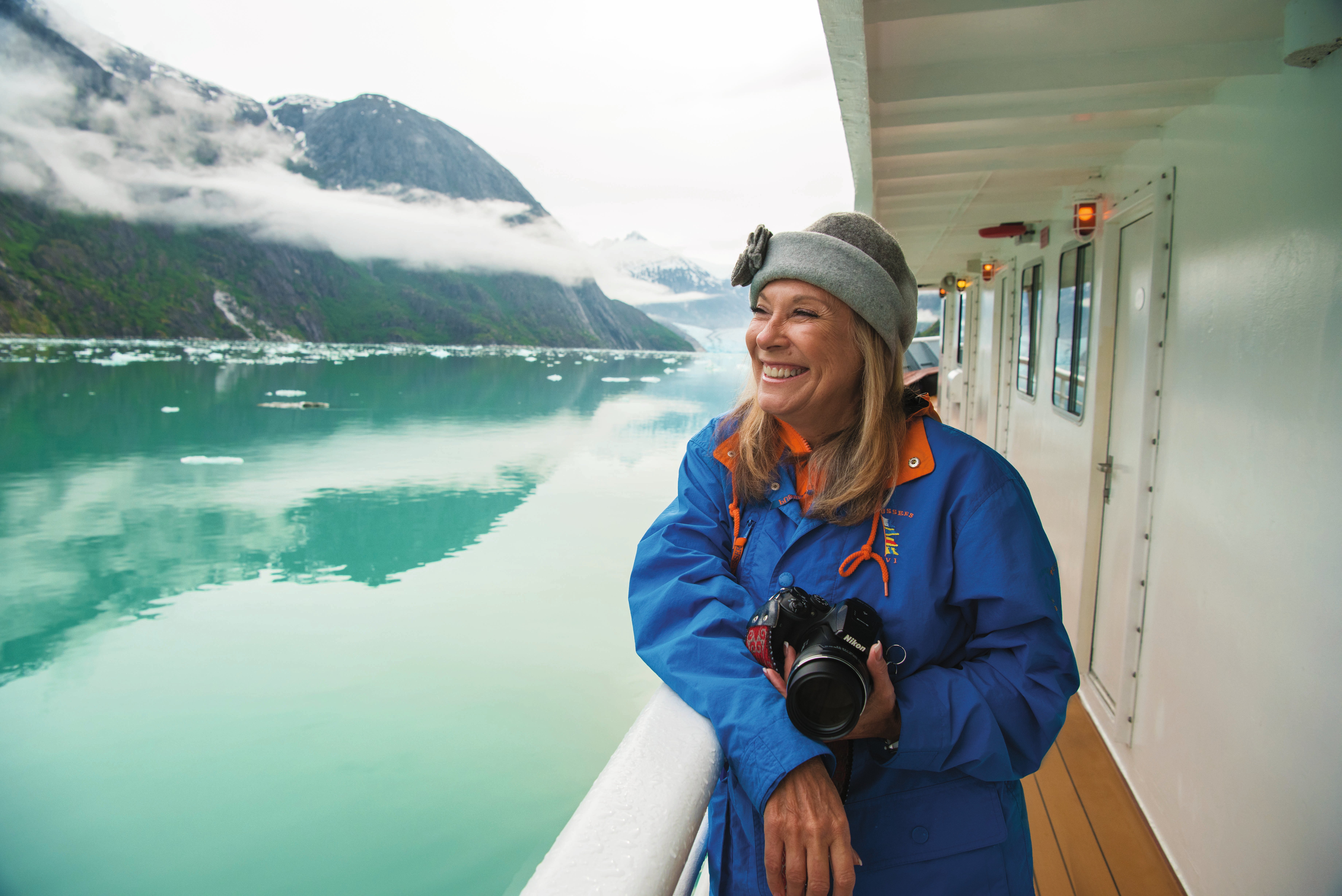 A woman holds a camera and smiles while looking out into Endicott Arm, Alaska.