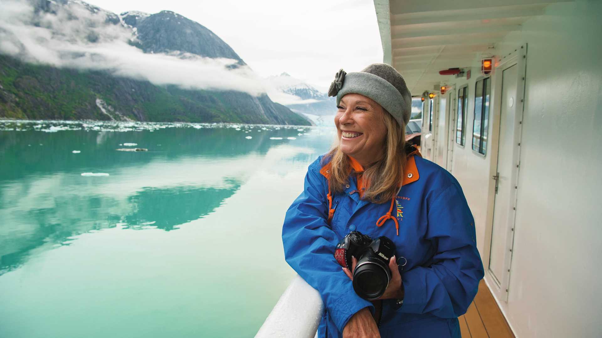 A woman holds a camera and smiles while looking out into Endicott Arm, Alaska.