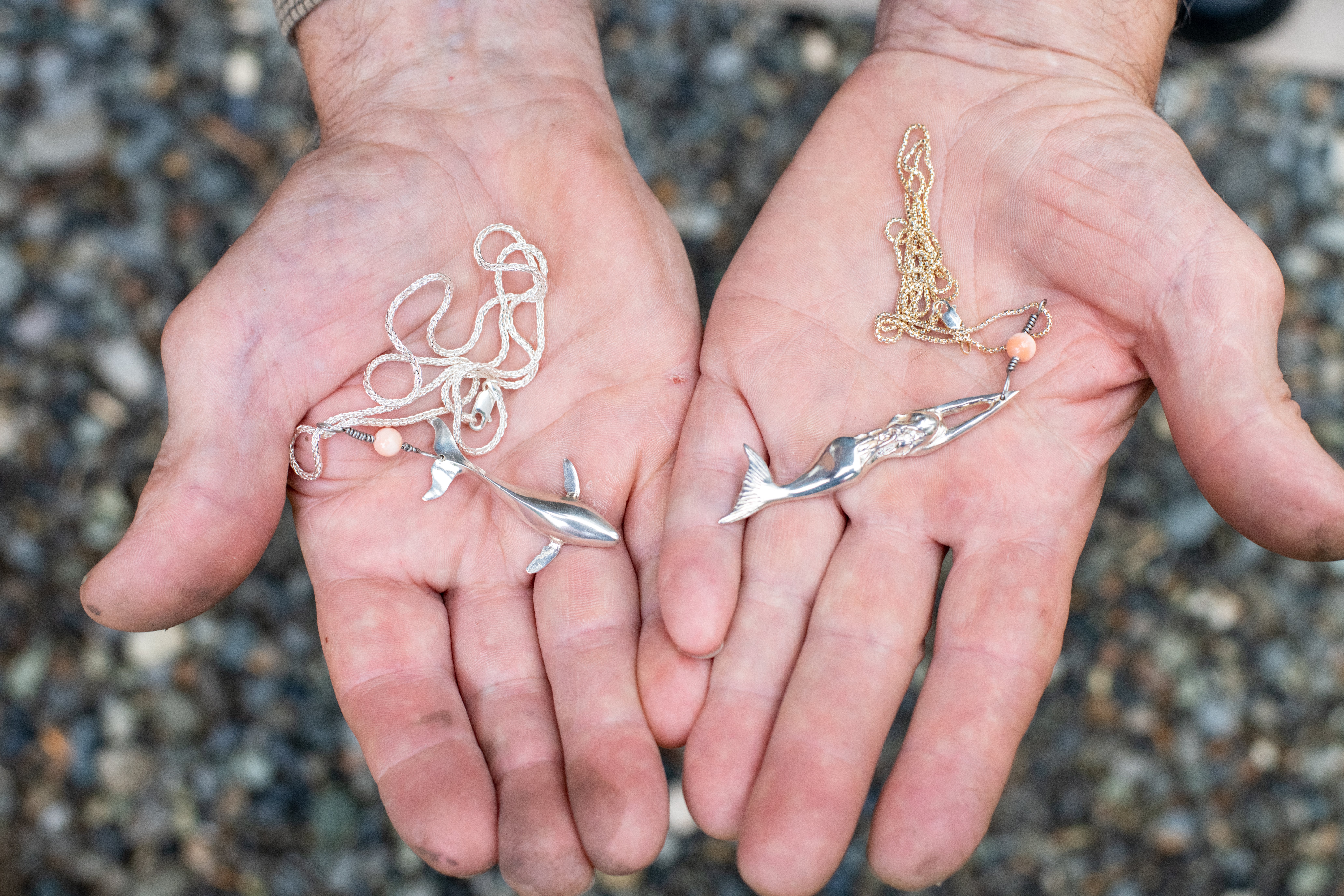 Two hands holding two necklaces.