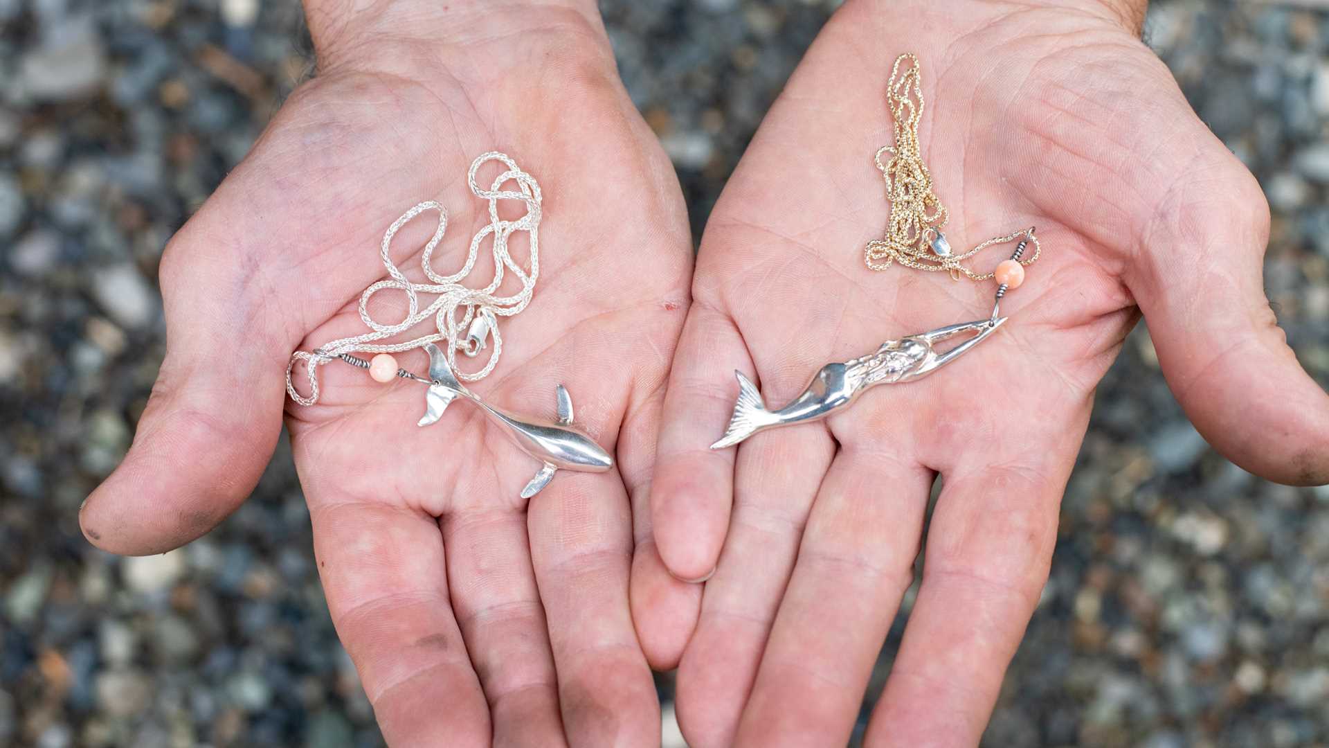 Two hands holding two necklaces.