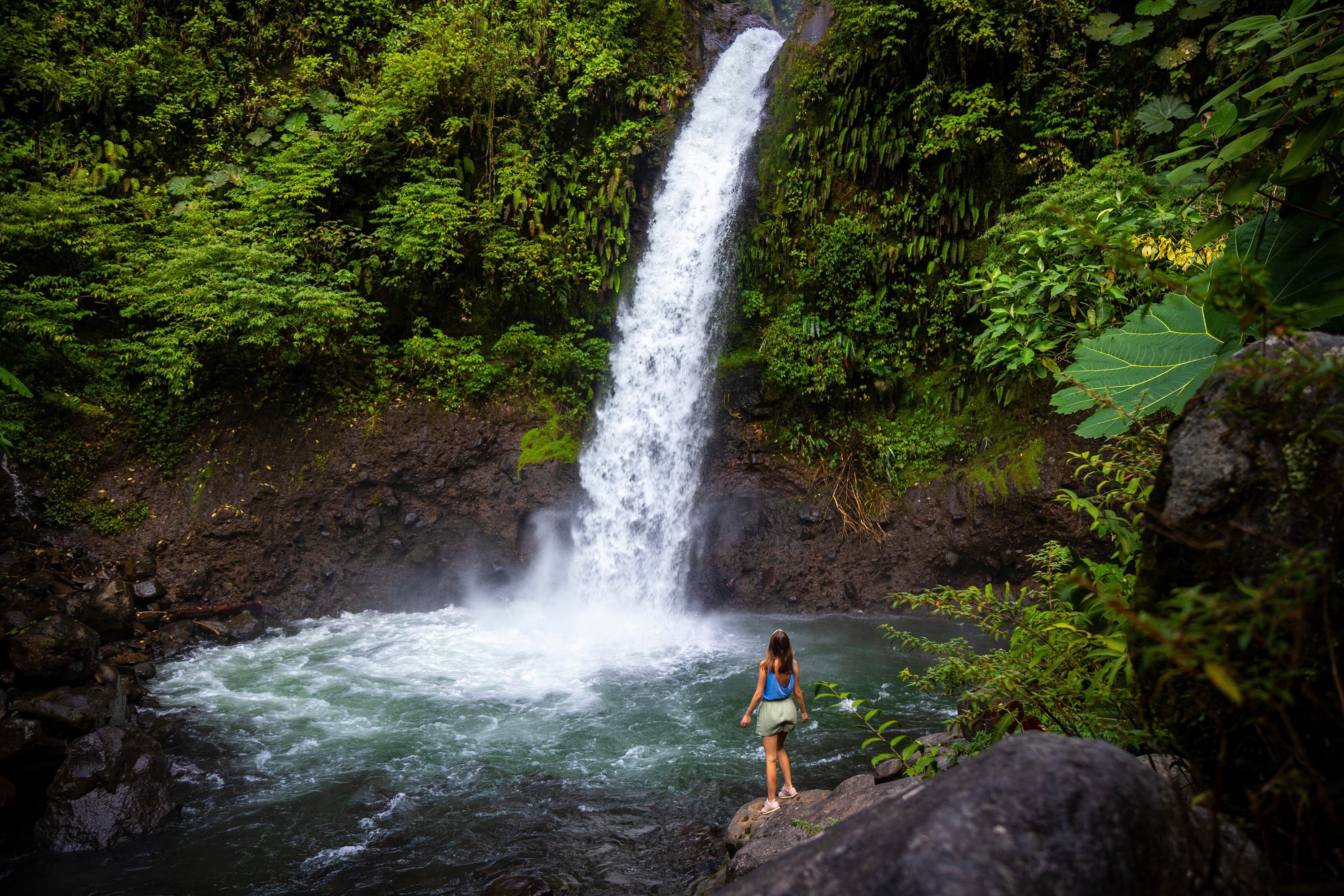 Woman standing on a rock near the bottom of a waterfall in Costa Rica.