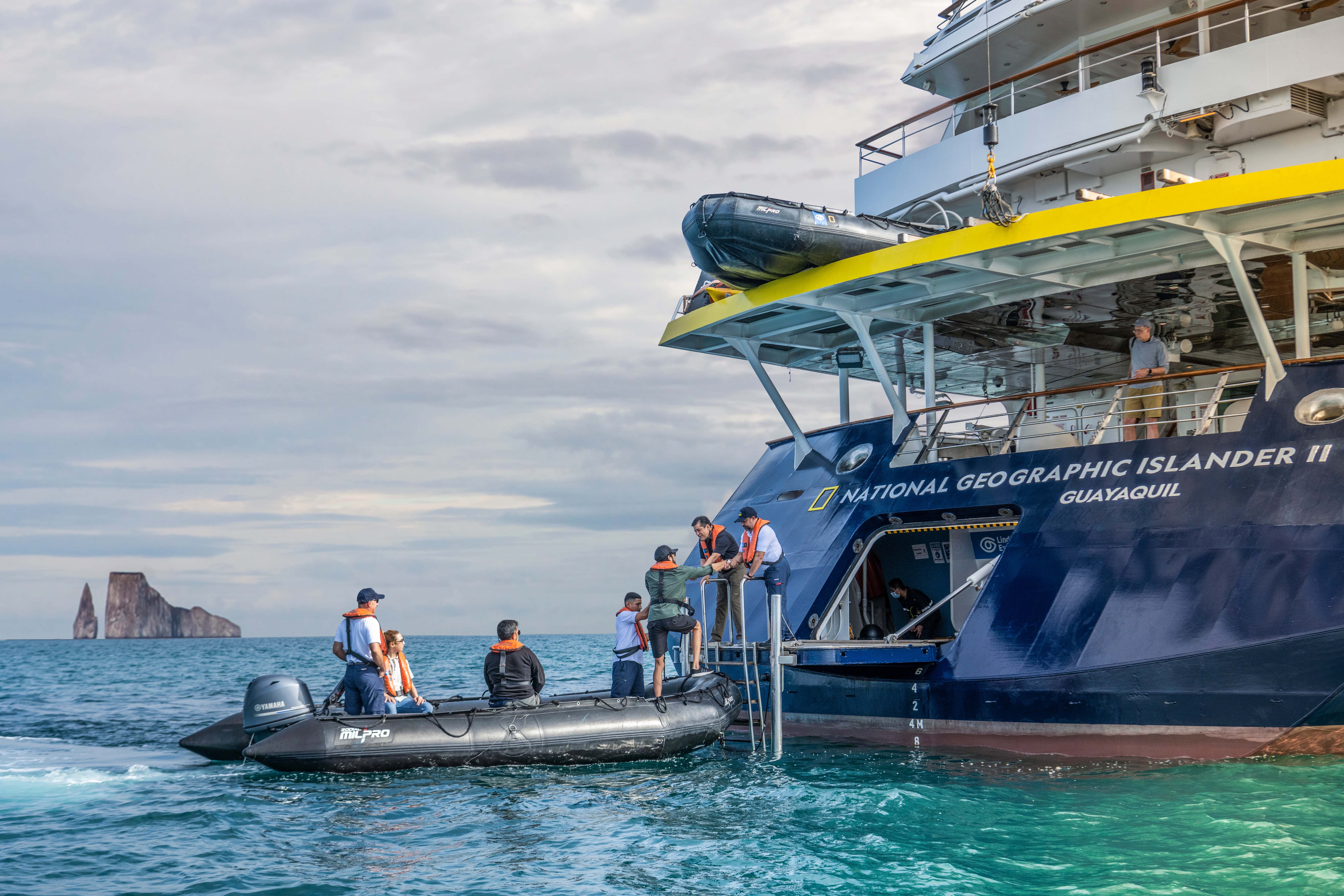 Staff from the ship National Geographic Islander II help a guest disembark a Zodiac boat at the ship's stern.