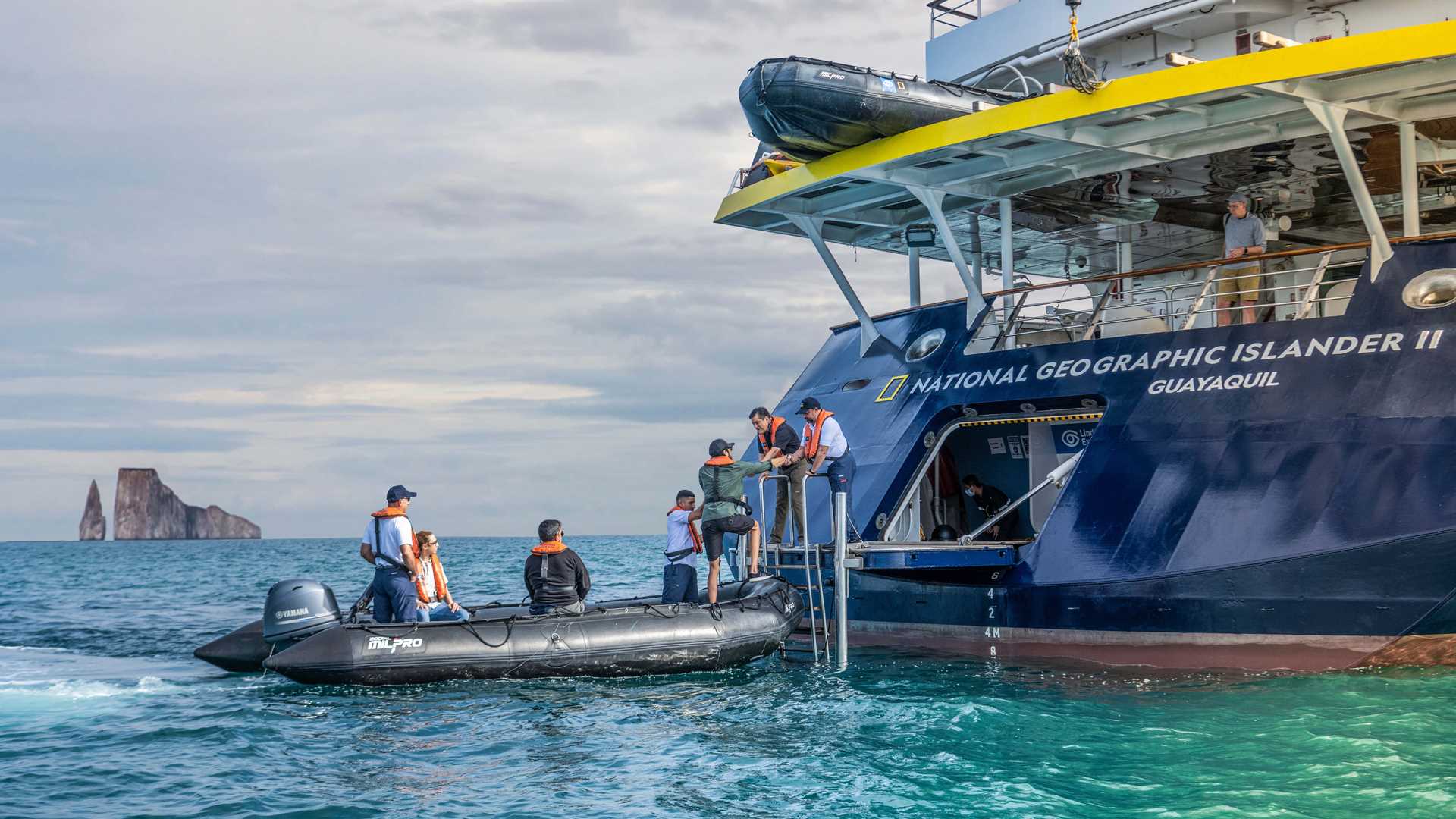 Staff from the ship National Geographic Islander II help a guest disembark a Zodiac boat at the ship's stern.