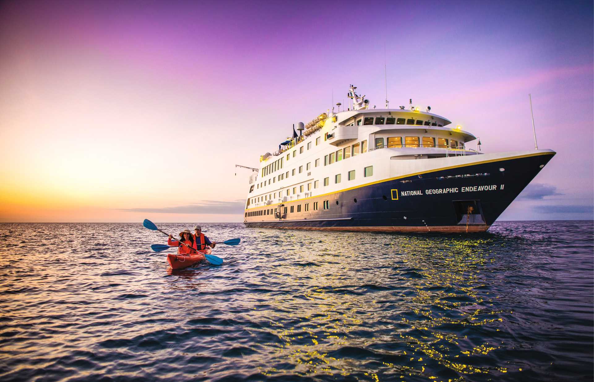 Two guests kayak during sunset near the ship National Geographic Endeavour II