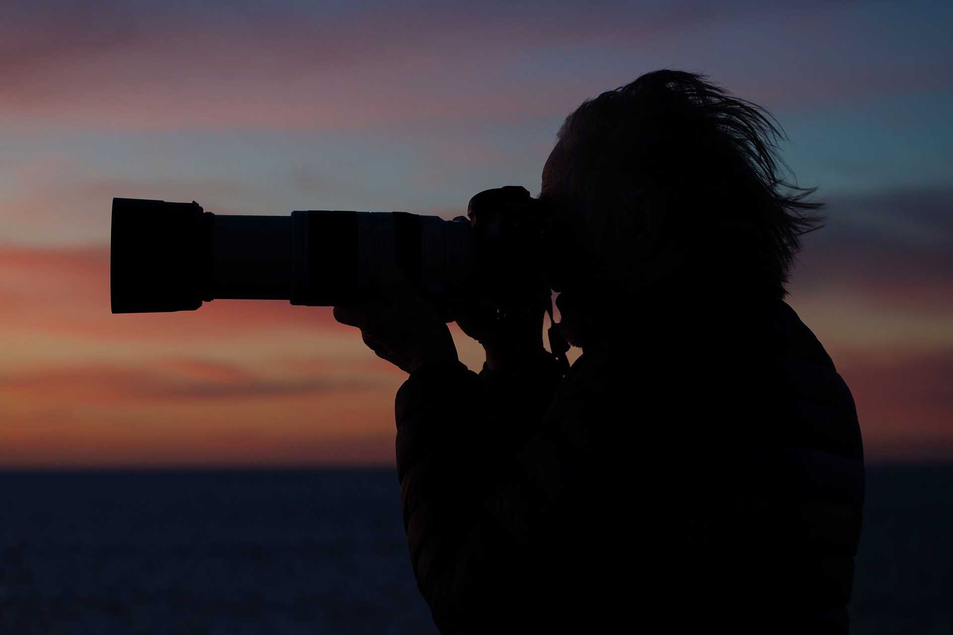 a silhouette of a man taking a photo of a sunrise