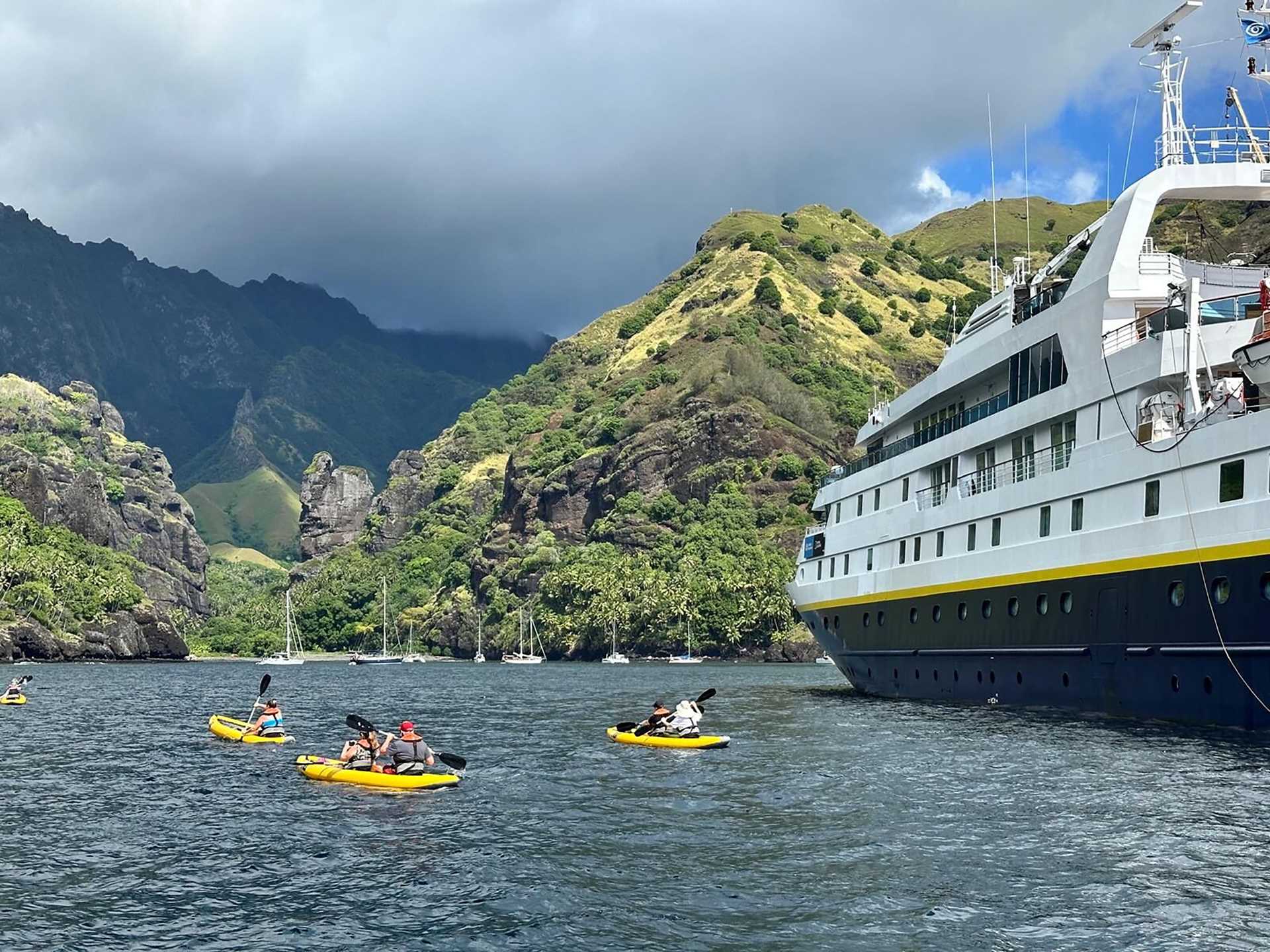 yellow kayaks in the water next to a blue and white ship with a green polynesian island in the background