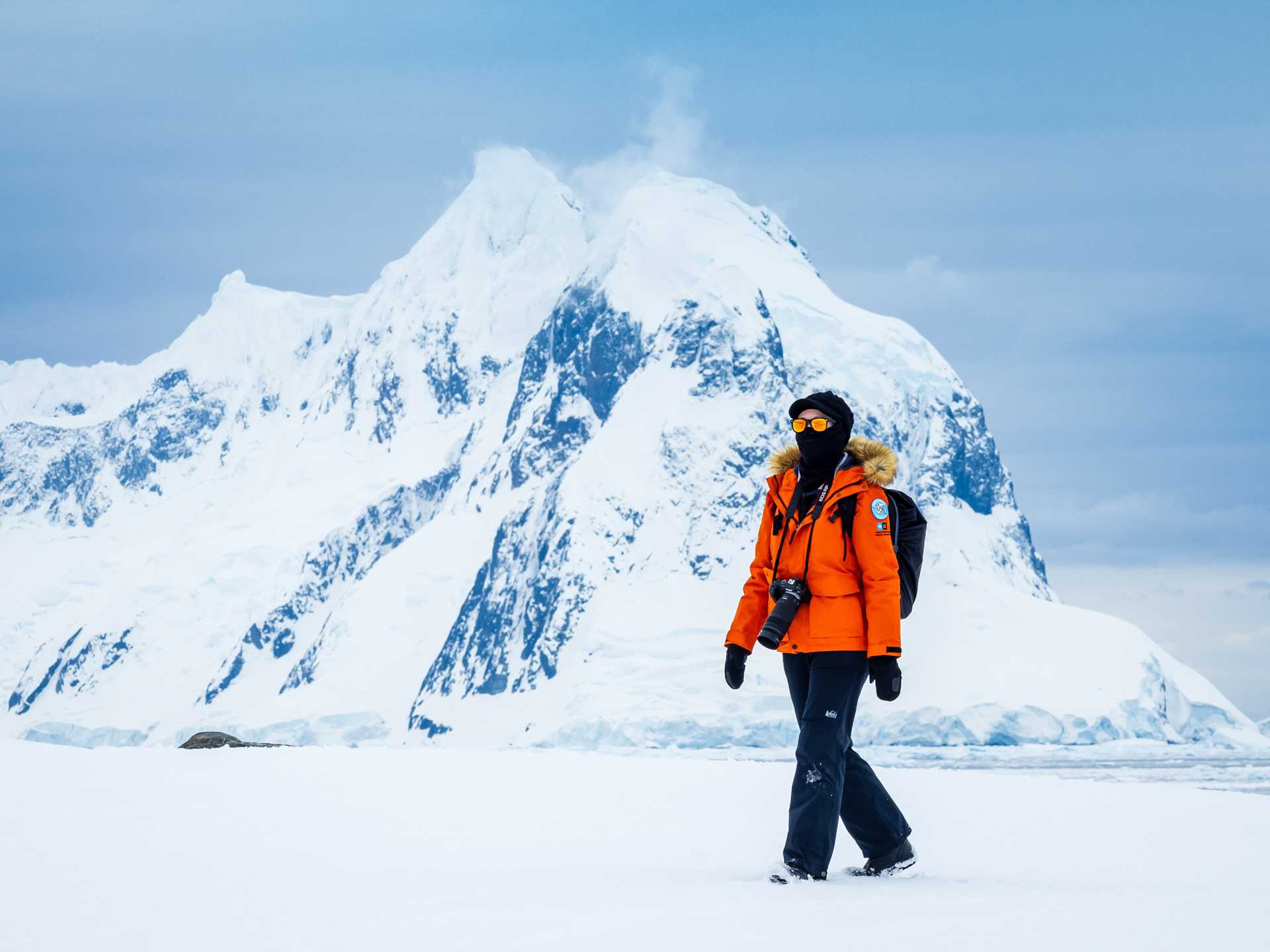 A traveler hikes on icy terrain on Peterman Island with snowy mountains in the background.