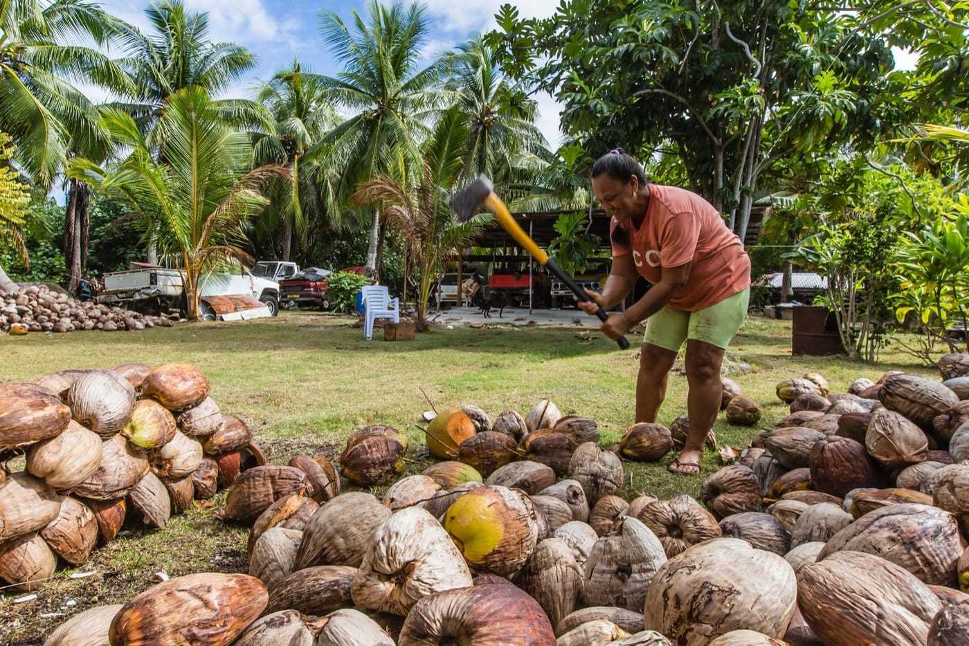 A man taking an axe to a large pile of coconuts with a smile on his face