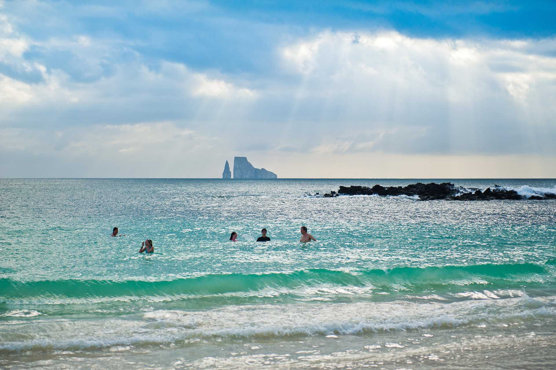 Five guests swim with a view of Kicker Rock in the distance, Galápagos Islands.