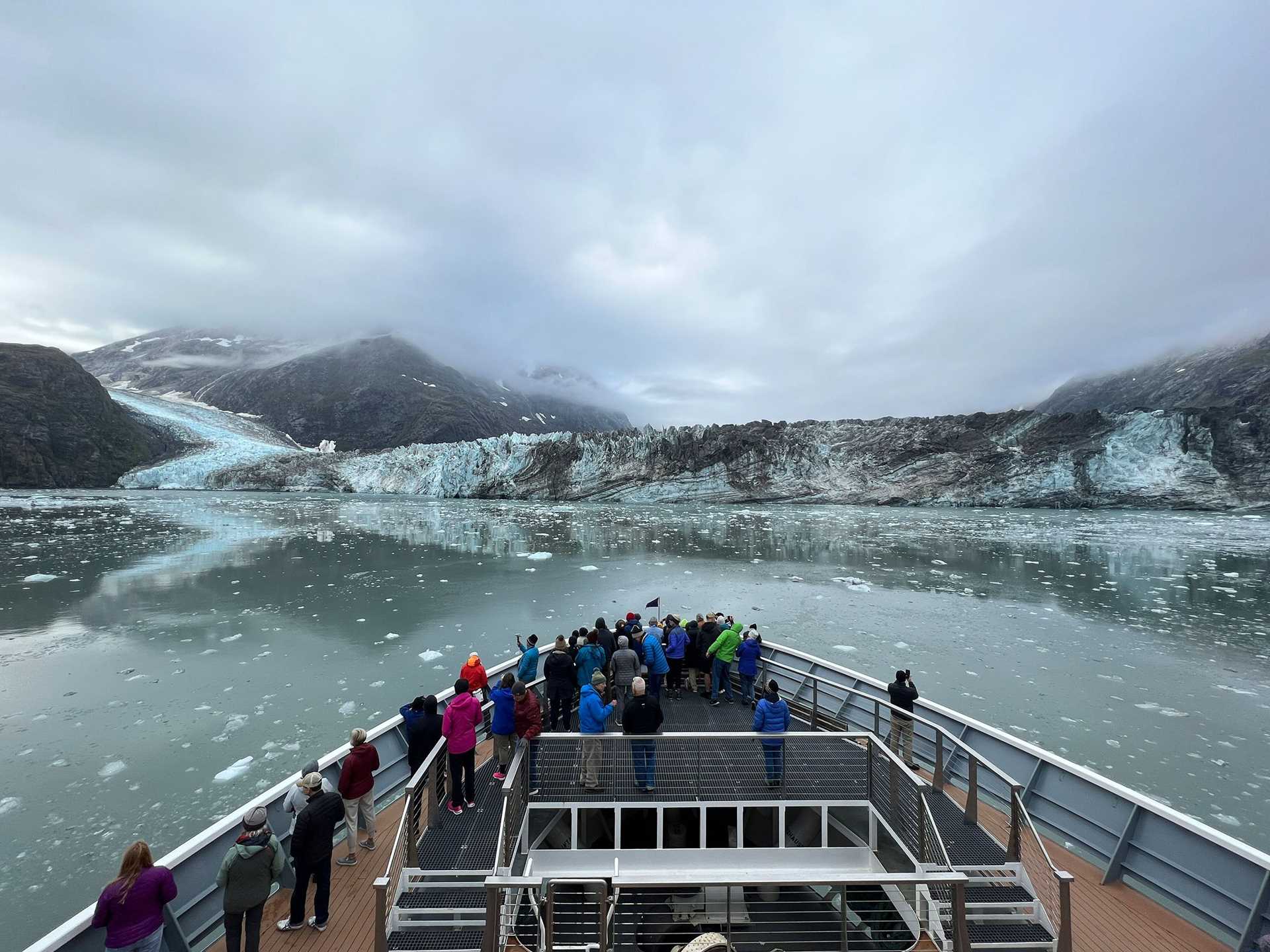 people standing on the bow of a ship with a glacier in the background