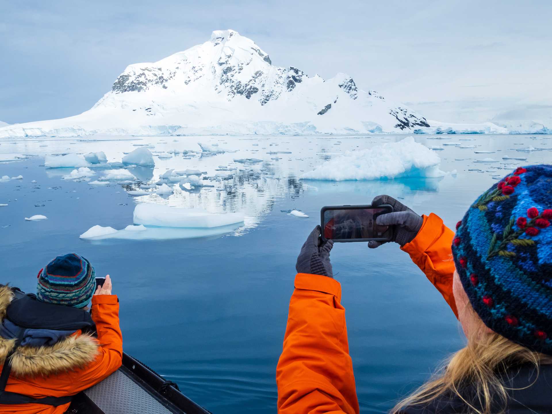 Two guests take photos on smartphones of the icebergs and mountains in Paradise Harbour.