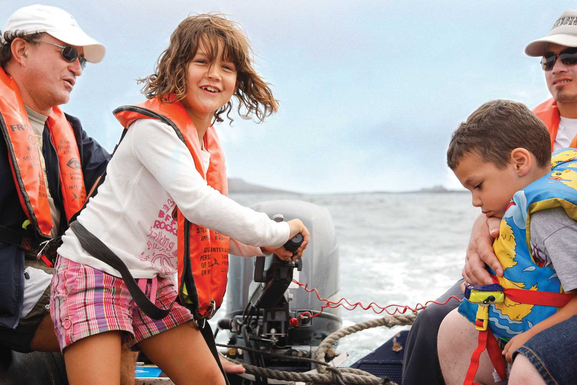 A child drives a Zodiac in Galápagos with adult supervision.